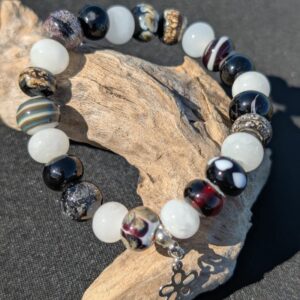 Bracelet en perles de verre noir et blanc aux motifs variés avec breloque fleur argentée